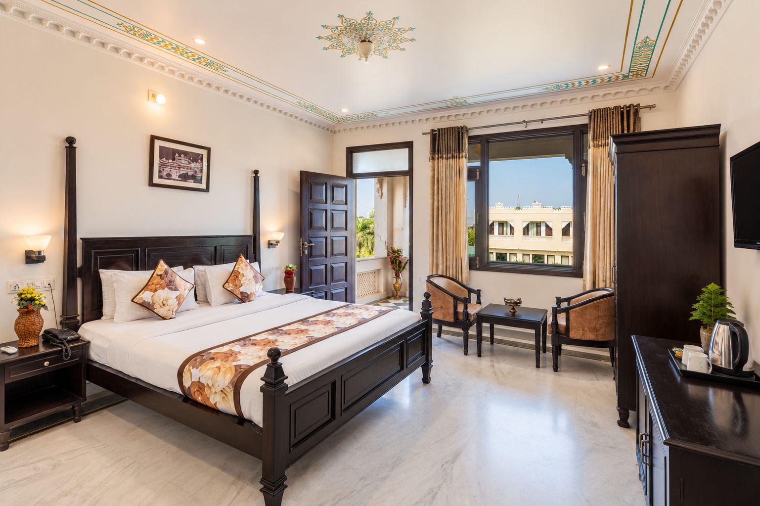 A hotel room with a large bed, bedside tables, a desk with chairs, a TV, and a window with a view.
