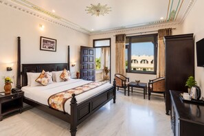 Quarto de hotel com cama grande, mesas de cabeceira, escrivaninha com cadeiras, televisão e janela com vista.
