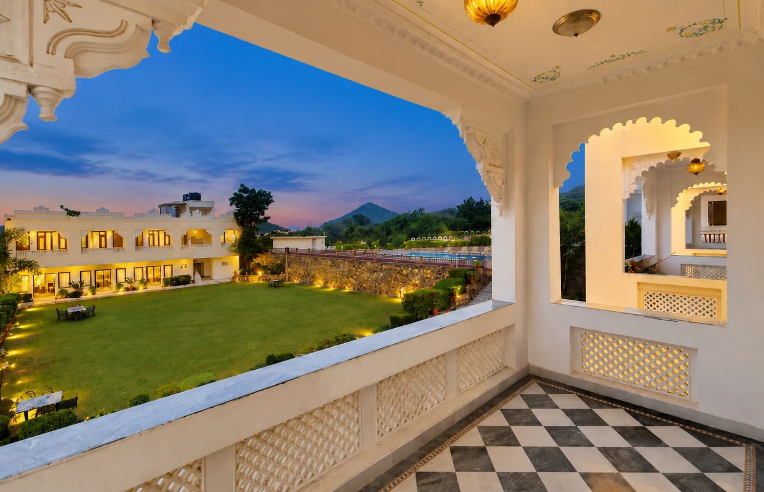 A hotel balcony with a checkered floor, a view of a well-lit courtyard, and traditional architectural elements.