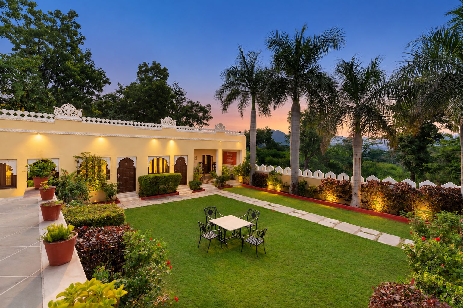 A courtyard with a dining table and chairs, surrounded by potted plants and palm trees.