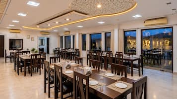 A spacious dining area with multiple tables and chairs, large windows, and a decorative ceiling.