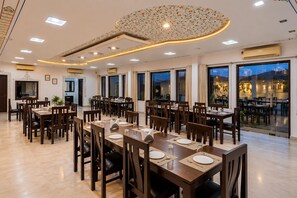 Un comedor amplio con varias mesas y sillas, ventanas grandes y un techo decorativo.