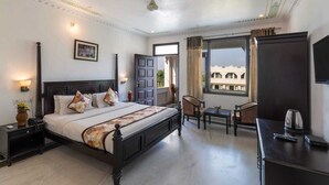 Una habitación de hotel con una cama grande, mesitas de noche, un escritorio, una silla, un televisor y una ventana con vistas a edificios.
