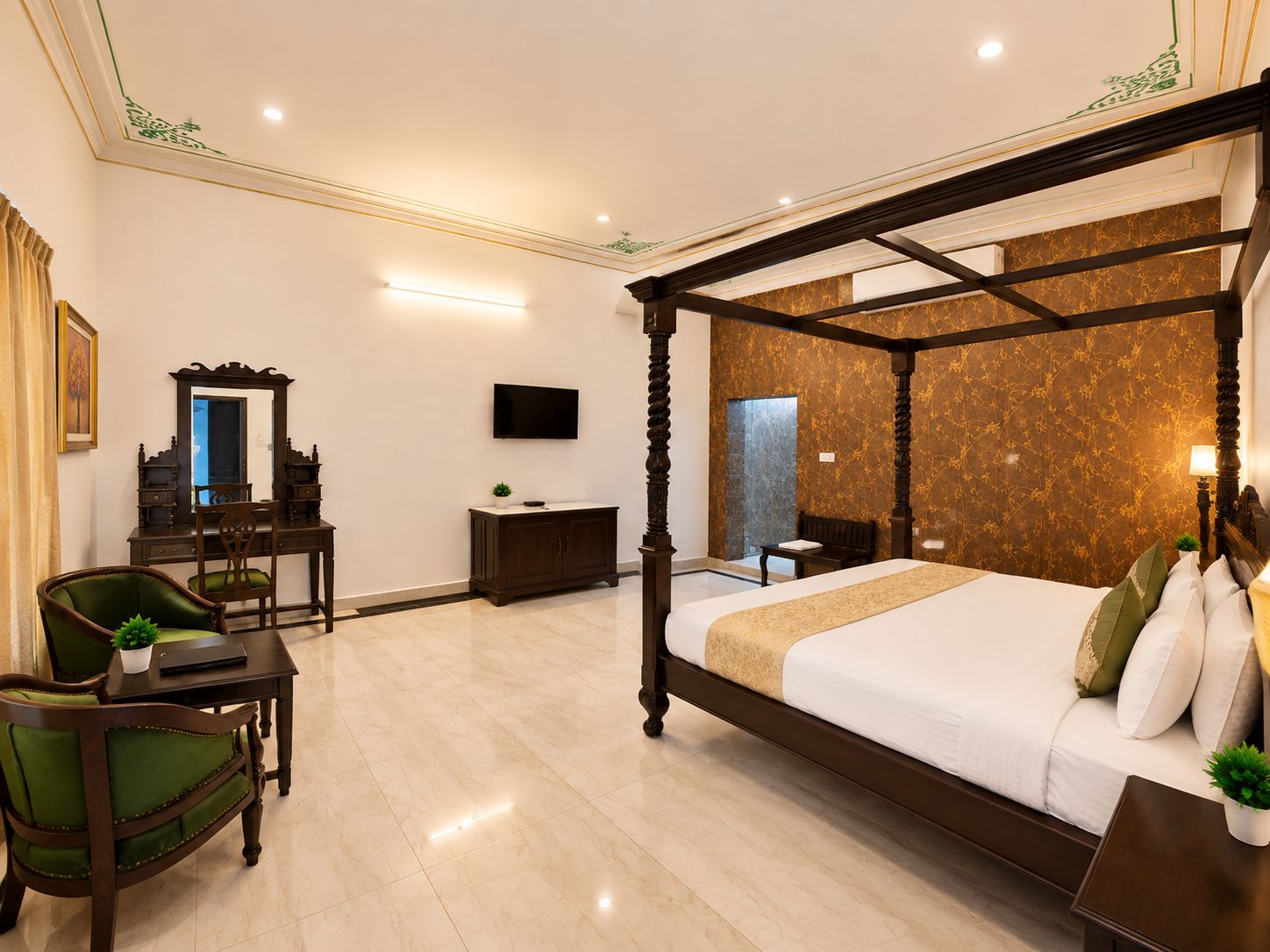 A four-poster bed with a headboard, a desk with a mirror, a television mounted on the wall, and a green upholstered chair.