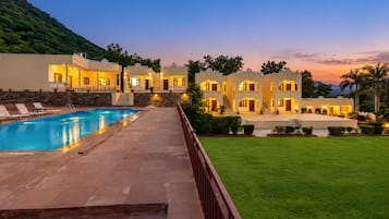 A hotel with a swimming pool, multiple guest rooms, and a well-maintained lawn.