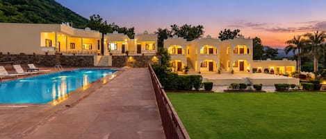 A hotel with a swimming pool, multiple guest rooms, and a well-maintained lawn.