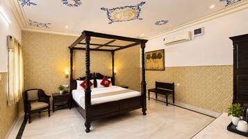 A four-poster bed with a nightstand, a chair, and a small table with a plant and cups.