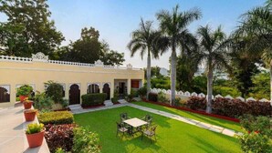 Un patio con césped, una mesa y sillas, y un edificio con arcos y una valla blanca.