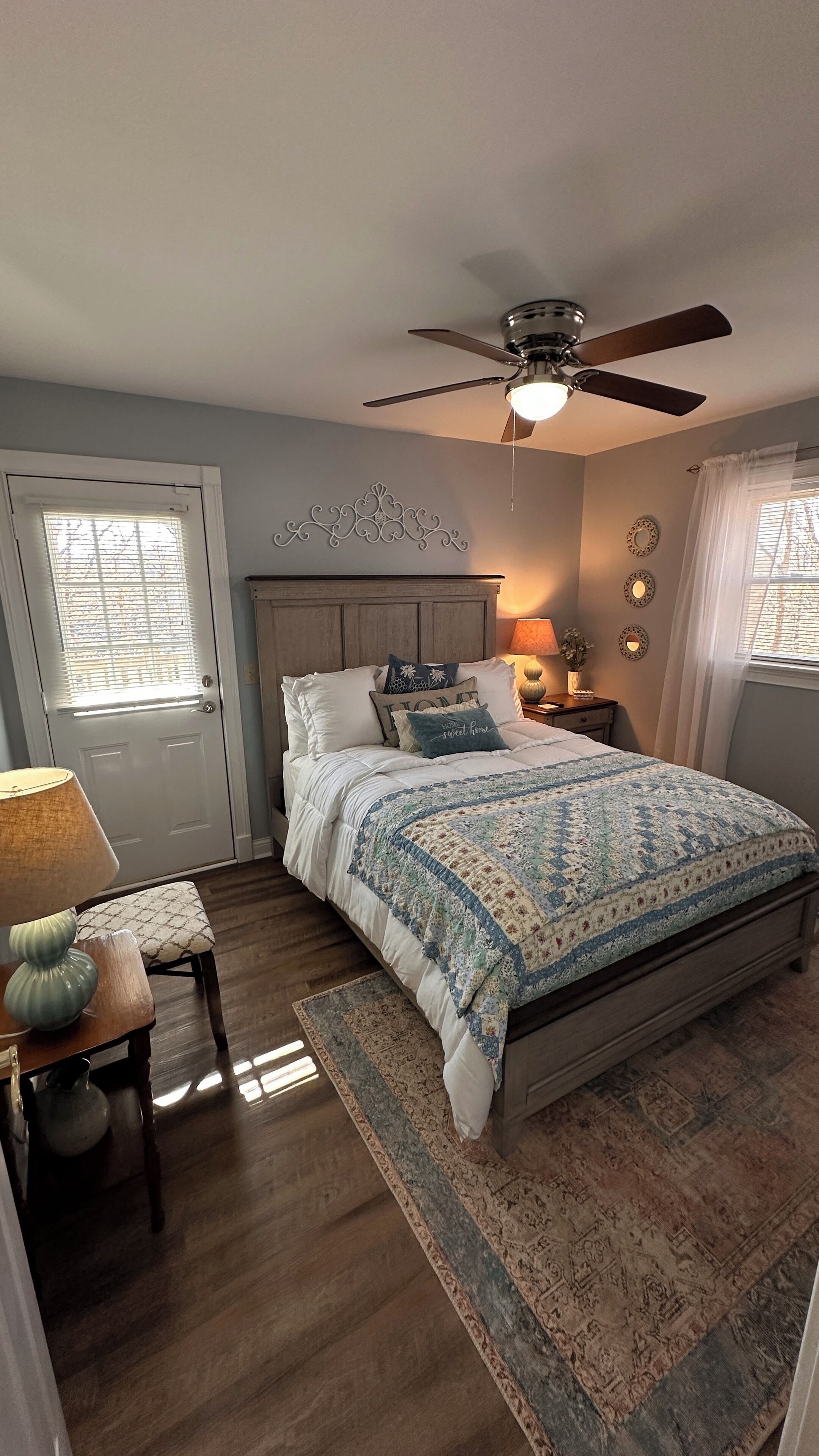 A bedroom with a bed, a ceiling fan, a nightstand, a lamp, a chair, and a window with blinds.