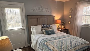 A bedroom with a bed, a ceiling fan, a nightstand, a lamp, a chair, and a window with blinds.