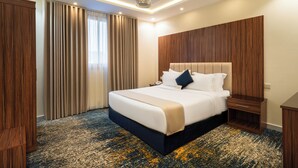 Ein Hotelzimmer mit einem großen Bett, einem hölzernen Kopfteil, einem Nachttisch, einem Schreibtisch und Teppichboden.