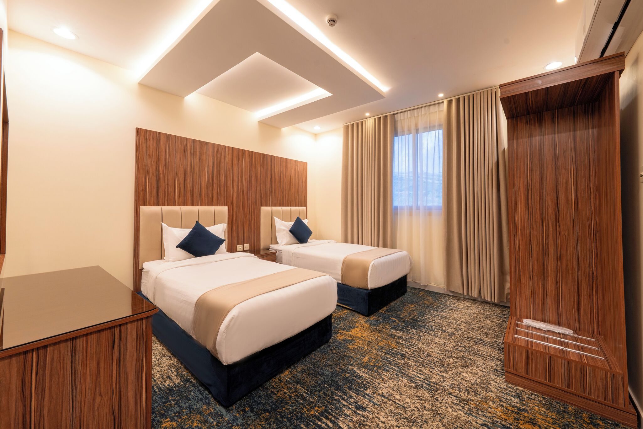Ein Hotelzimmer mit zwei Betten, einem hölzernen Kopfteil, einem großen Spiegel und einem Teppichboden.