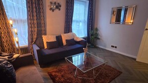 A living room with a sofa, a glass coffee table, and a potted plant. - 1BR Sleeps6 Elizabethline Ws98 (London)