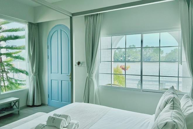 Habitación de hotel con cama, ventana con vistas a un cuerpo de agua, puerta y planta.