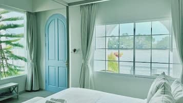Habitación de hotel con cama, ventana con vistas a un cuerpo de agua, puerta y planta.