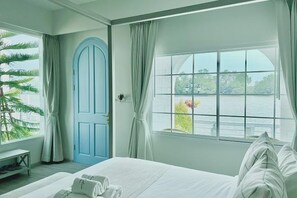Ein Hotelzimmer mit Bett, Fenster mit Blick auf ein Gewässer, einer Tür und einer Pflanze.