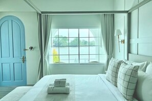Ein Hotelzimmer mit Bett, Blick auf ein Gewässer, einer blauen Tür und einem fenster mit Vorhängen.