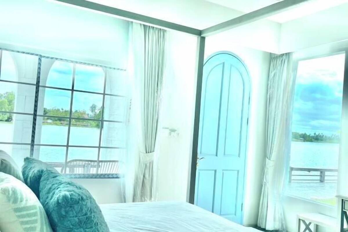 Une chambre avec une grande fenêtre, un lit et une porte bleue.