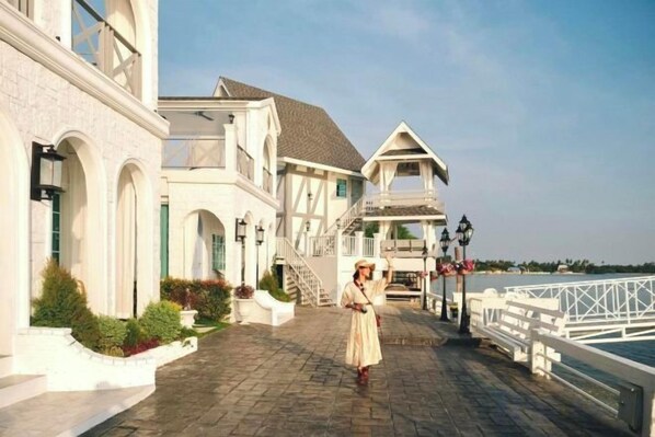 A waterfront property with a paved walkway, a white fence, and a building with a gabled roof. - Prima Amphawa (Mueang Samut Songkhram)