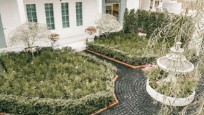 A white building with a paved courtyard, a fountain, and neatly arranged greenery. - Prima Amphawa (Mueang Samut Songkhram)