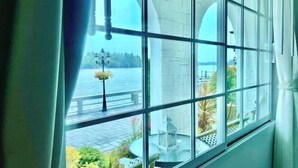 A view through a window with a view of a body of water, a stone structure, and outdoor seating. - Prima Amphawa (Mueang Samut Songkhram)