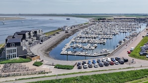 A marina with boats docked, a parking area, and a building with large windows. - Apartment in Zeeland by Oosterschelde Beach (Sint-Annaland)