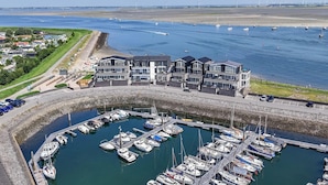 A marina with multiple boats docked, a large building with a modern design, and a clear view of the water and distant wind turbines. - Apartment in Zeeland by Oosterschelde Beach (Sint-Annaland)