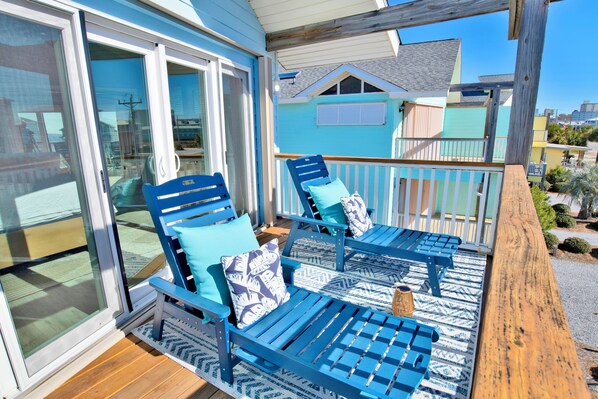 A wooden deck with two blue lounge chairs and a small table, overlooking a residential area.