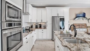 A modern kitchen with white cabinets, stainless steel appliances, and a marble countertop.