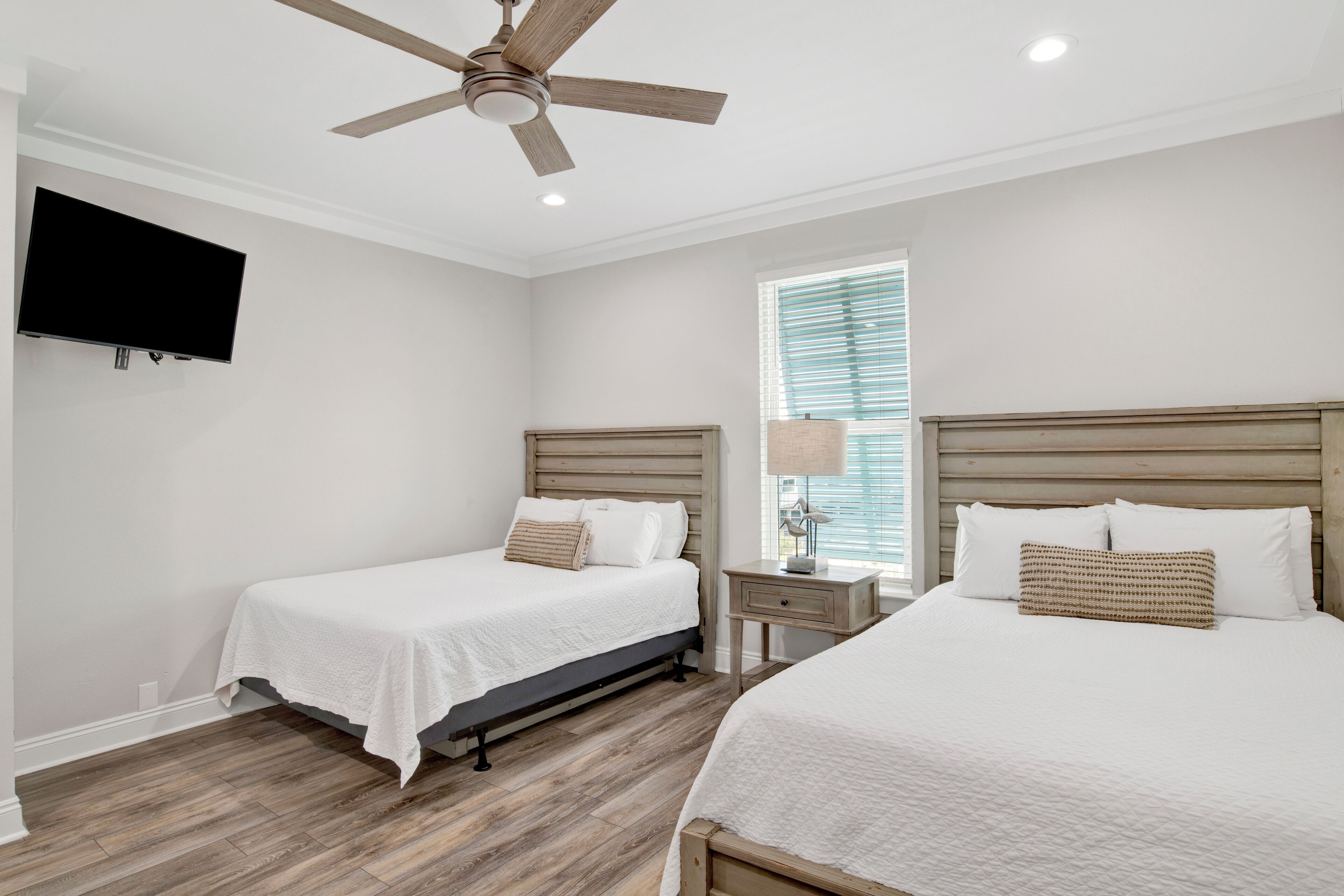 A bedroom with two beds, a ceiling fan, a TV, and a window with blinds.