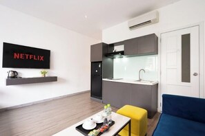 Ein modernes Wohnzimmer mit Flachbildfernseher, einer kleinen Küchenzeile und einem Sofa.