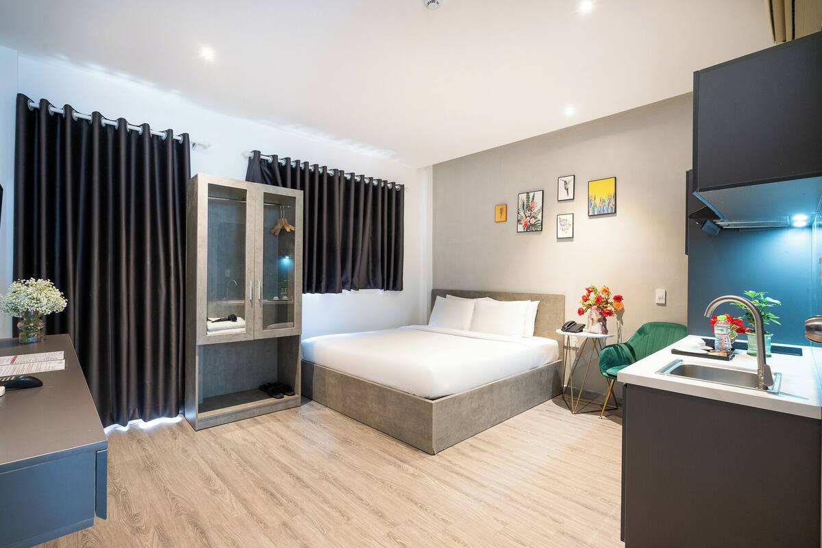 Une chambre d’hôtel moderne, dotée d’un grand lit, d’un bureau avec une chaise, d’une petite table agrémentée d’un vase de fleurs, et d’une salle de bain avec douche et lavabo.