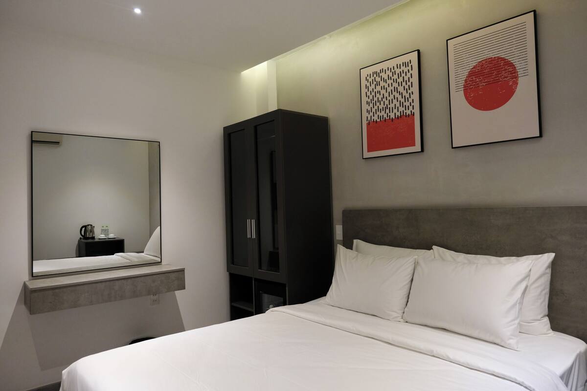 Une chambre d’hôtel moderne équipée d’un grand lit, d’une armoire, d’une table de chevet et d’un miroir.