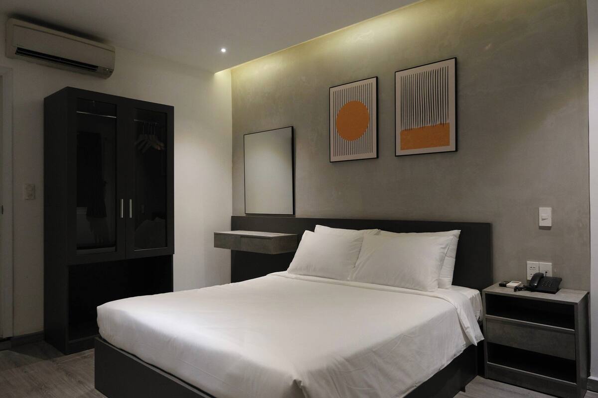Une chambre d’hôtel moderne dotée d’un grand lit, d’une armoire, d’une table de chevet avec un téléphone et de deux œuvres d’art accrochées au mur.