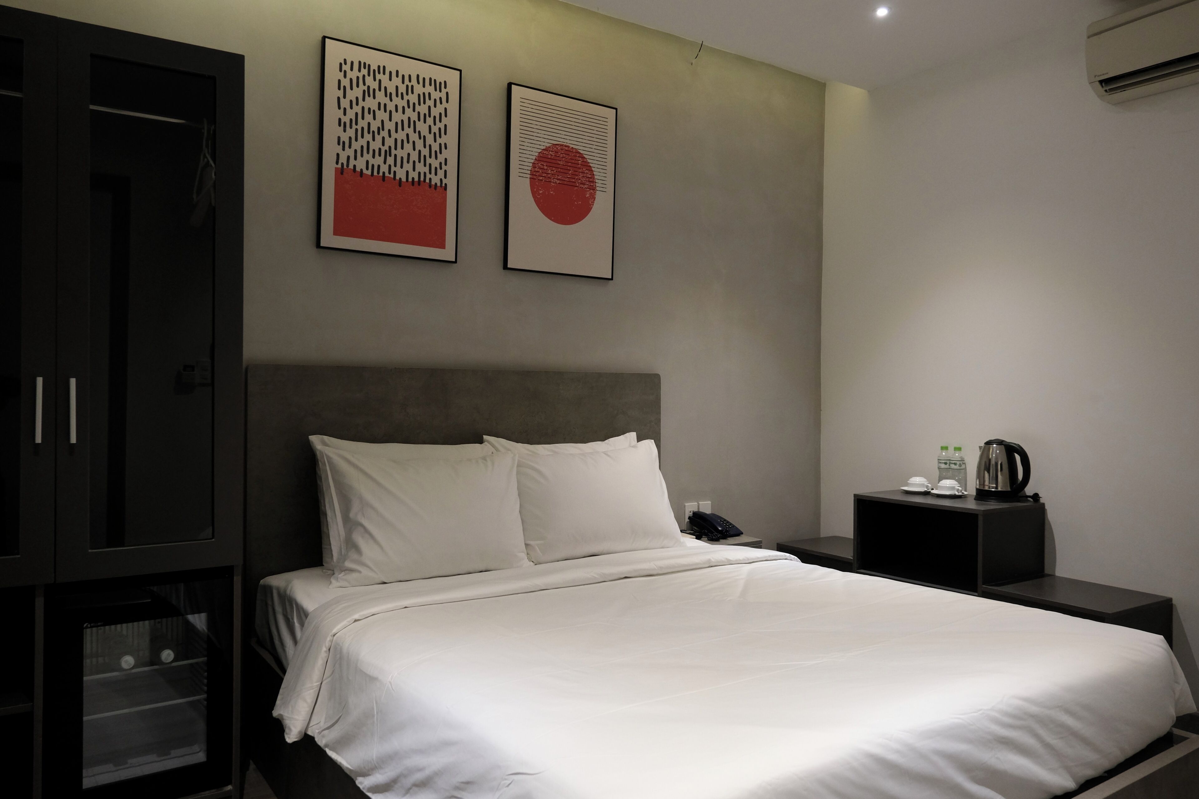 Ein Hotelzimmer mit einem Bett, einem Nachttisch, einem Schrank und zwei an der Wand befestigten Kunstwerken.