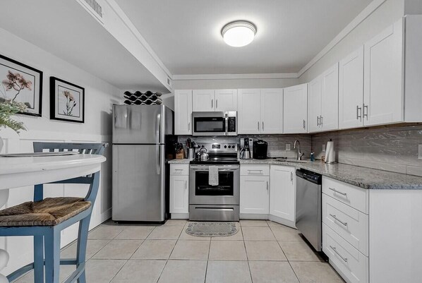 A modern kitchen with white cabinets, stainless steel appliances, and a tiled floor. - Marsh Estate: 3-Units + Theater Room! Putting! (Murrells Inlet)