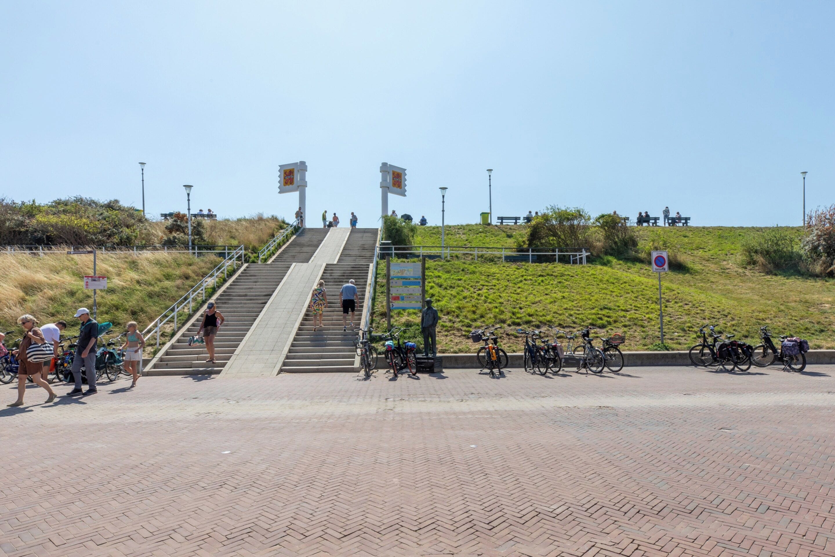 A paved pathway leading to a hill with a statue and benches.