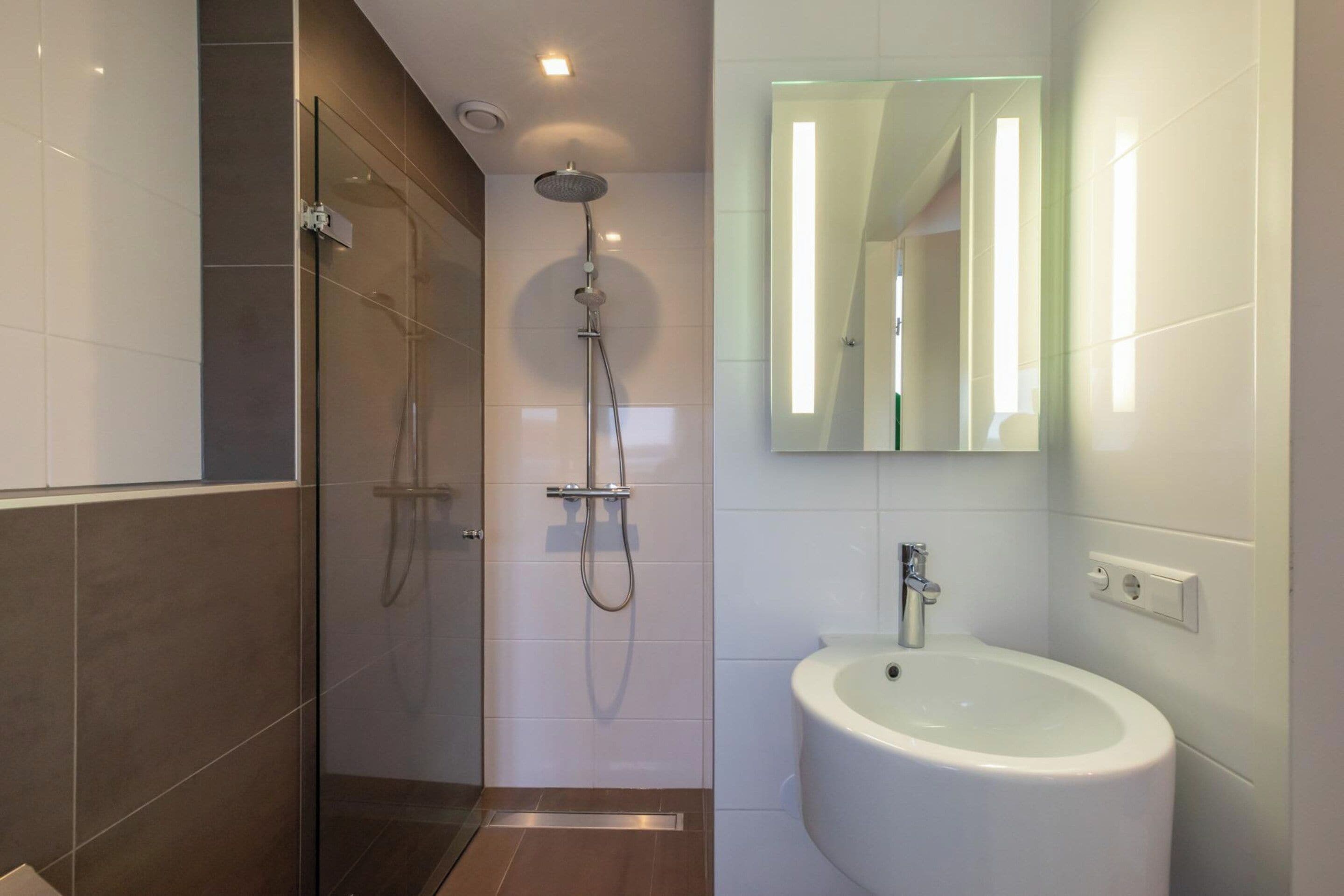 A modern bathroom with a glass-enclosed shower, a white sink, and a mirror with a light strip.