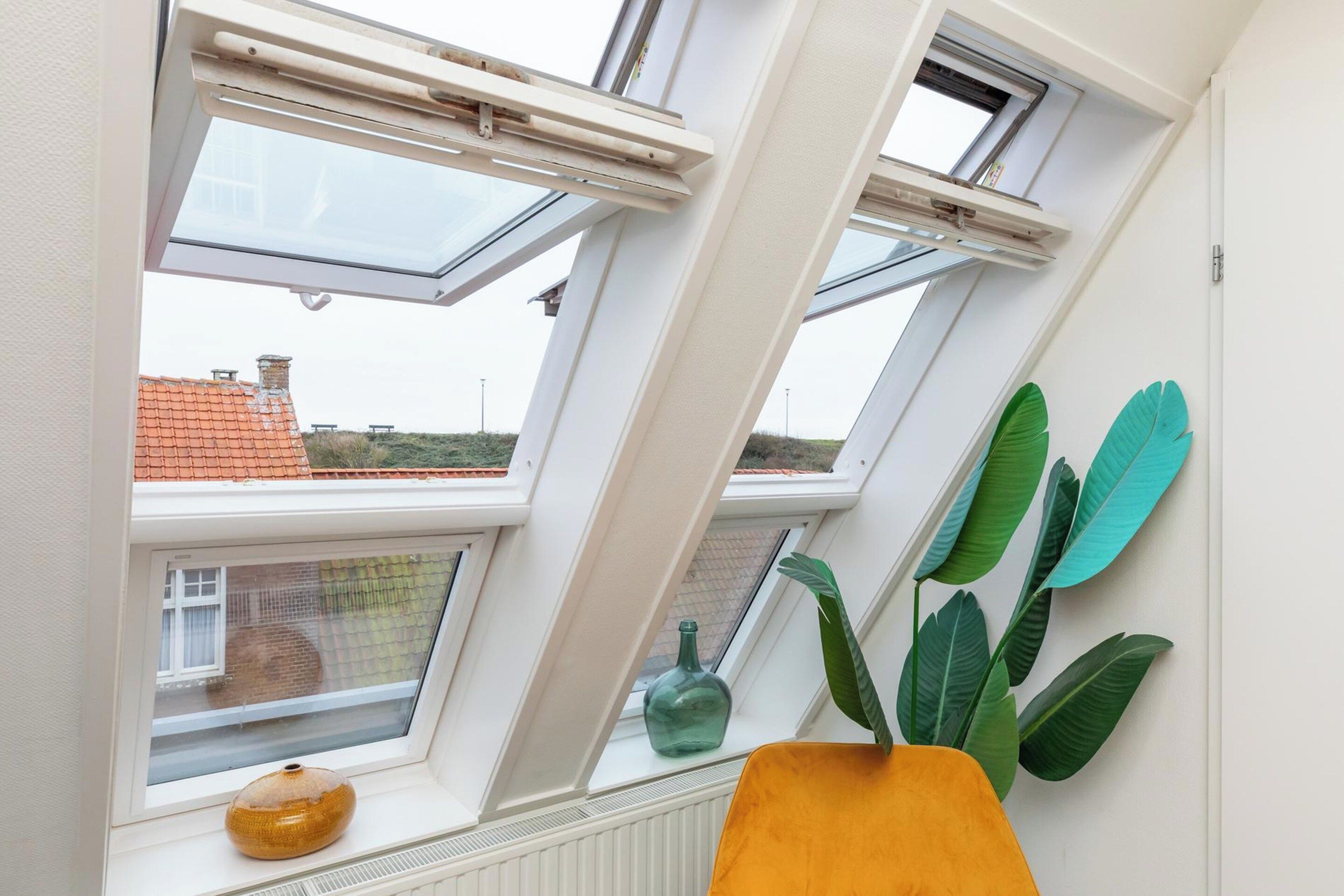 Une pièce dotée de fenêtres de toit, d’un radiateur, d’une fenêtre ornée d’un vase et d’une plante.