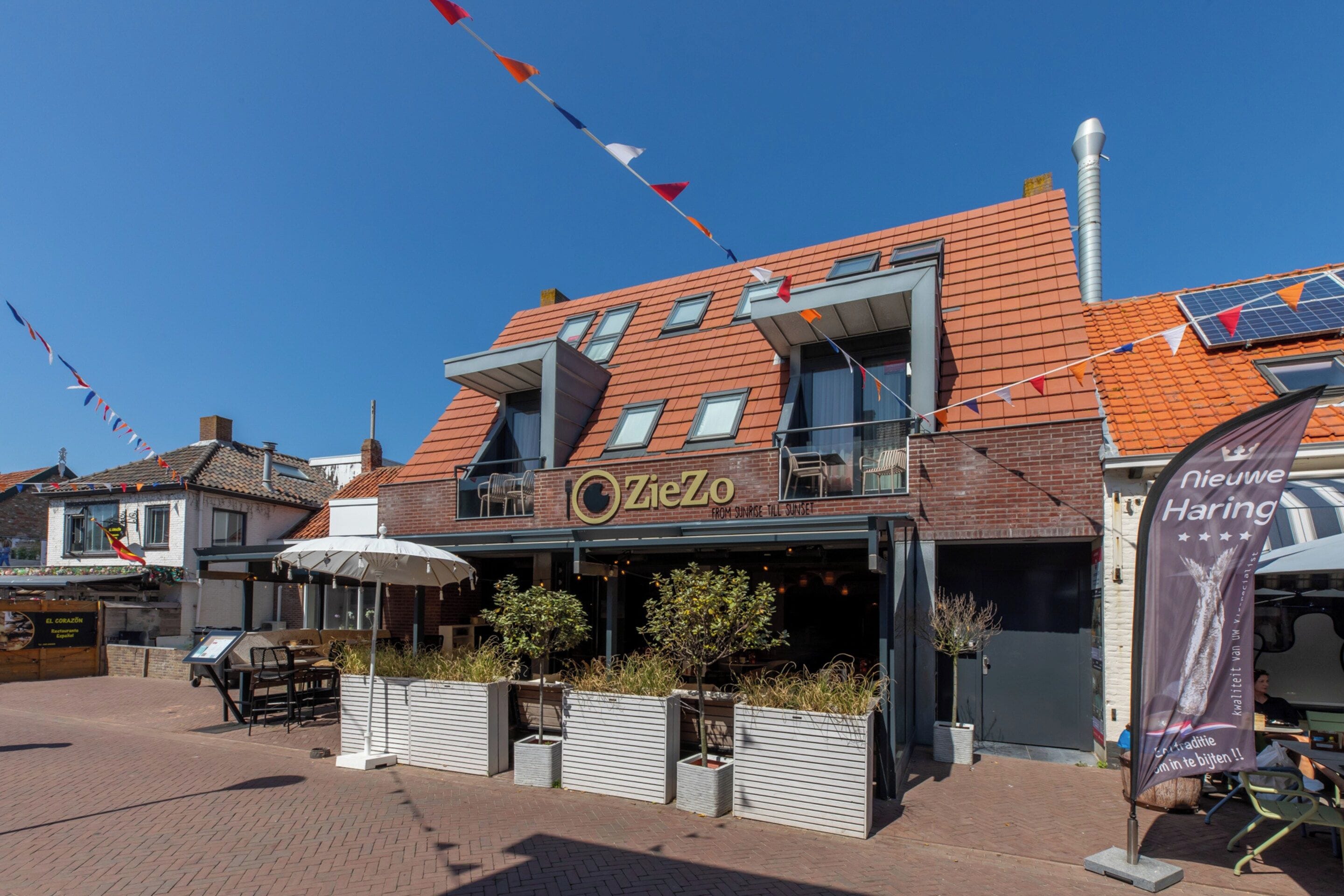 A building with a modern design, featuring a restaurant named 'ZieZo' with outdoor seating and a sign indicating it serves from sunrise till sunset.