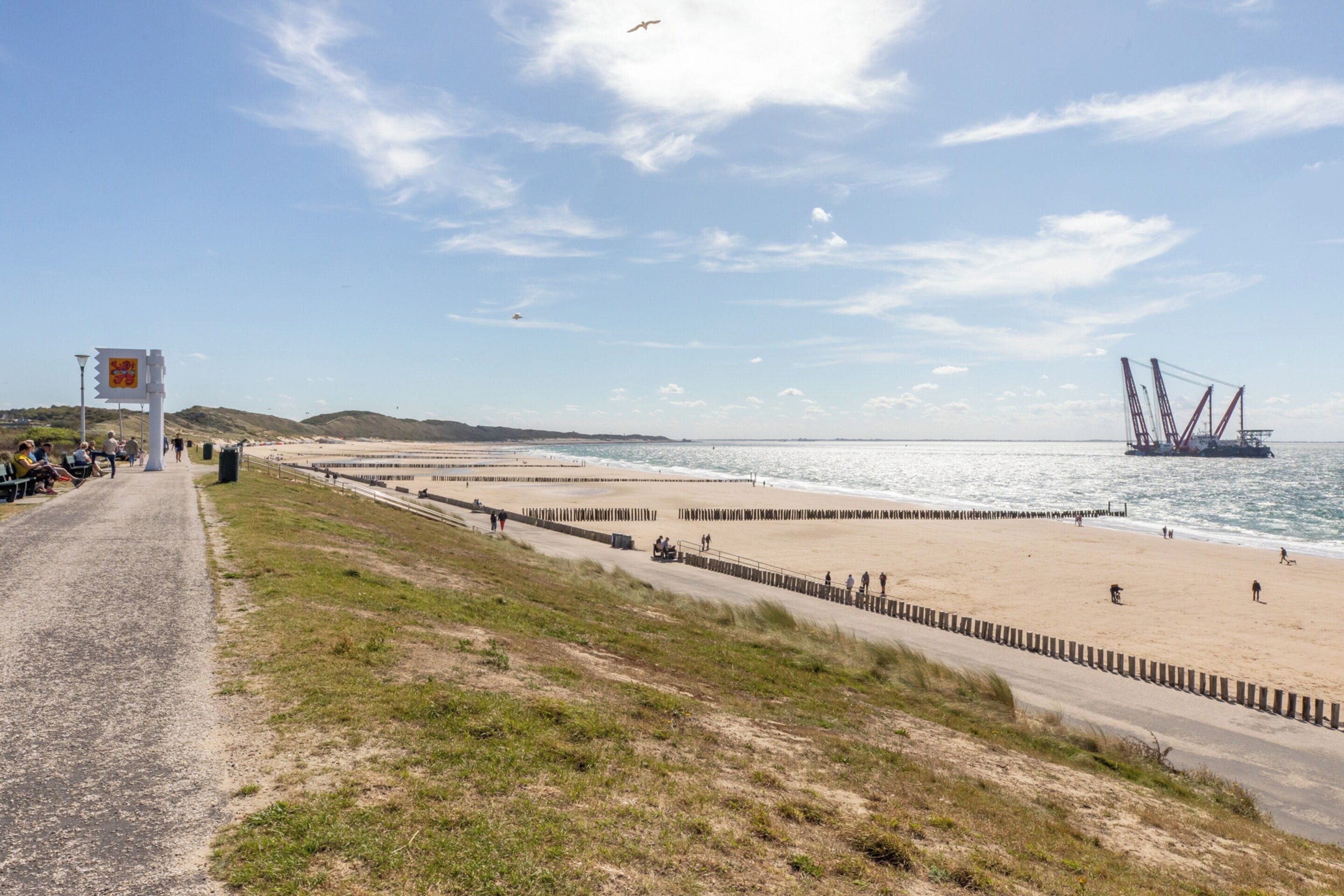 Une route c ôtière menant à une plage où se trouvent une jetée et une grande structure en forme de grue.
