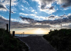 A paved pathway leading to a beach with a sunset in the background. - Cozy Couple's Escape (Zoutelande)