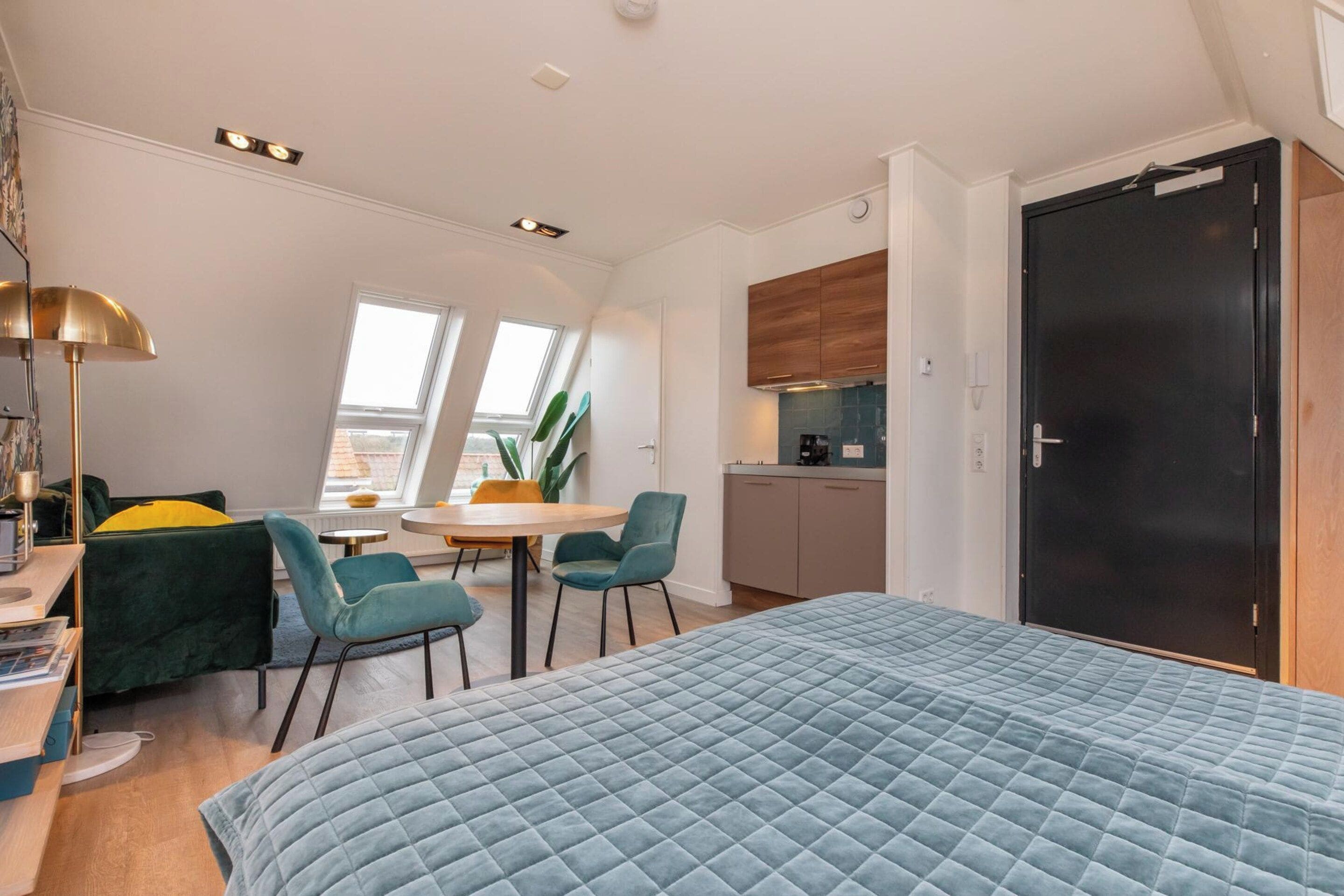 Ein kleines Zimmer mit einem Bett, einem Schreibtisch, einem Stuhl, einem Esstisch und einer Küchenzeile.