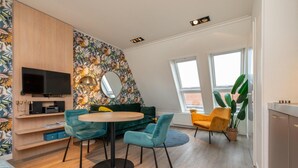 A modern living room with a round table, teal chairs, a green sofa, a TV, and a large mirror. - Cozy Couple's Escape (Zoutelande)