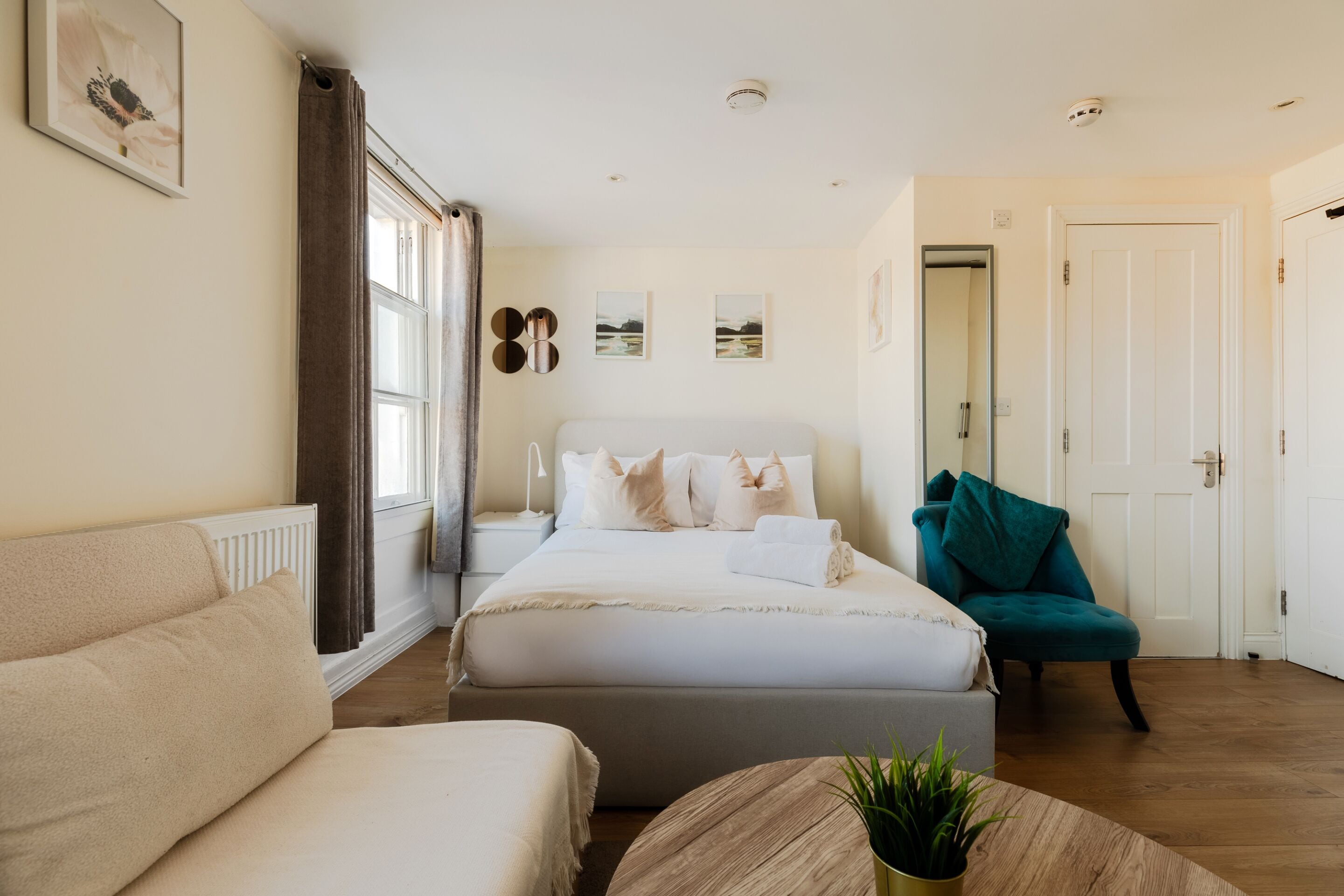 A bedroom with a bed, a sofa, a chair, and a round table with a plant.