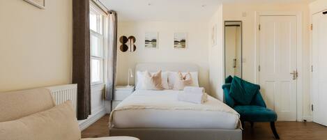 A bedroom with a bed, a sofa, a chair, and a round table with a plant.