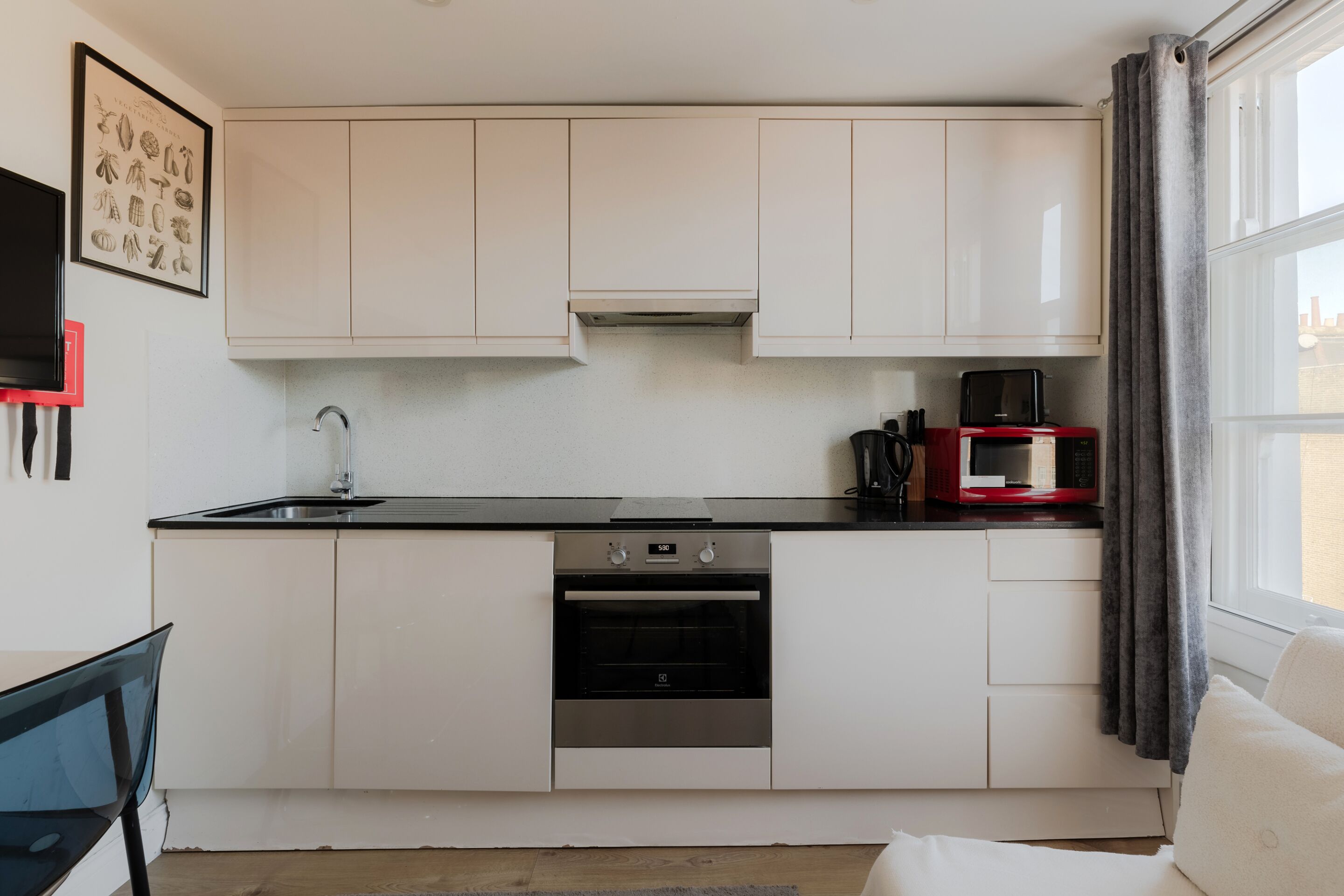 Cozinha compacta com armários brancos, forno de aço inoxidável, micro-ondas e pia.