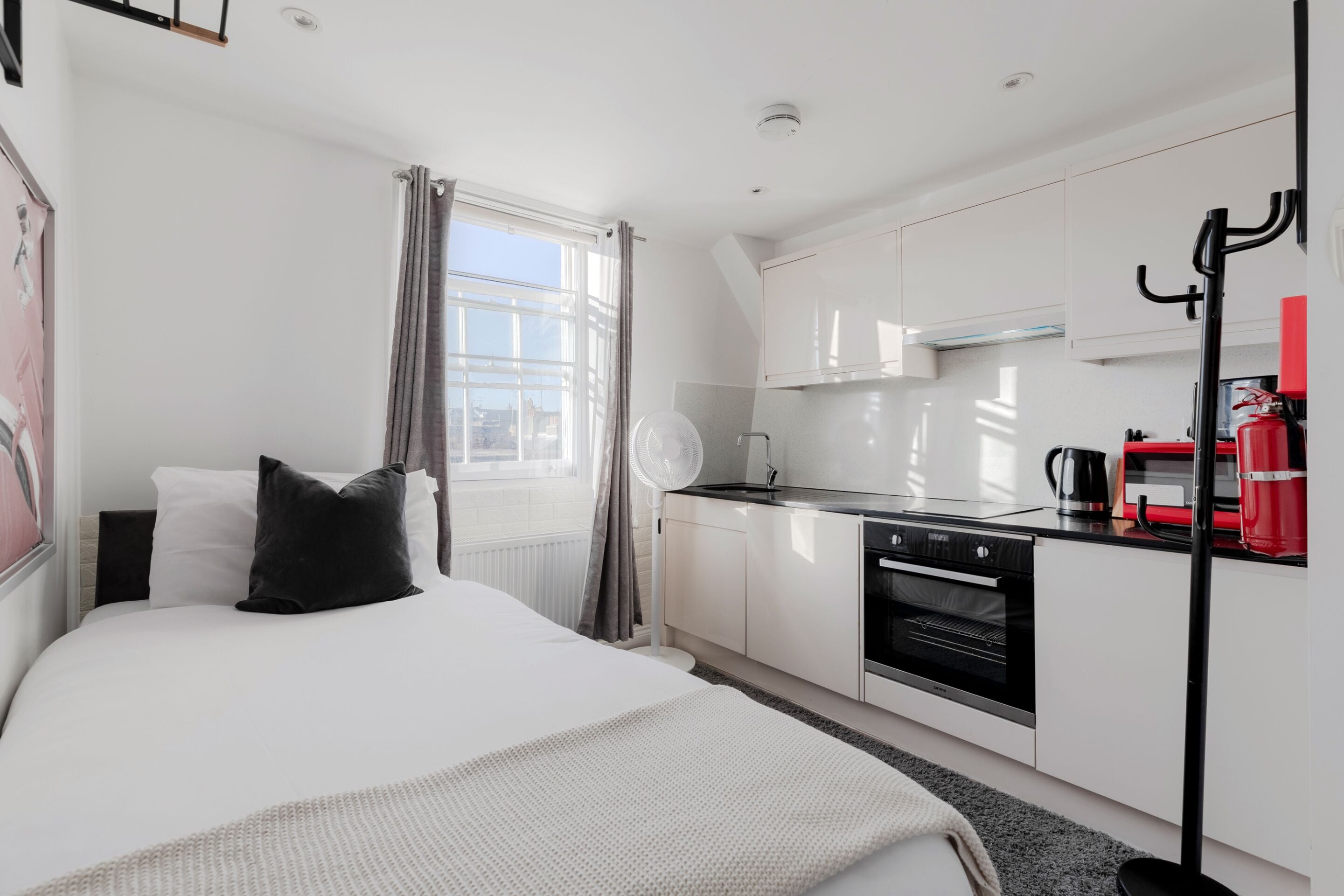 Ein modernes Hotelzimmer mit Bett, einer Küchenzeile, einem Fenster mit Vorhängen und Blick auf die Stadt.