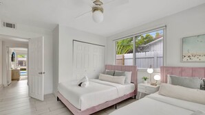 A bedroom with a bed, bedside table, and a window with a view of a fence and greenery. - Poolside Paradise Dock & Pool! (Oakland Park)