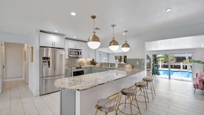 A modern kitchen with stainless steel appliances, a marble island, and bar stools. - Poolside Paradise Dock & Pool! (Oakland Park)